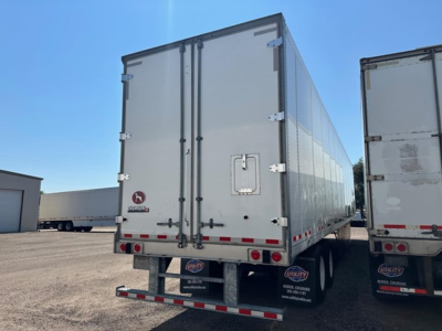 Trailer rear showing two swing doors, metal box, reflective tape, and standard rear bumper with lights. Branding stickers and license plate area not clearly legible.