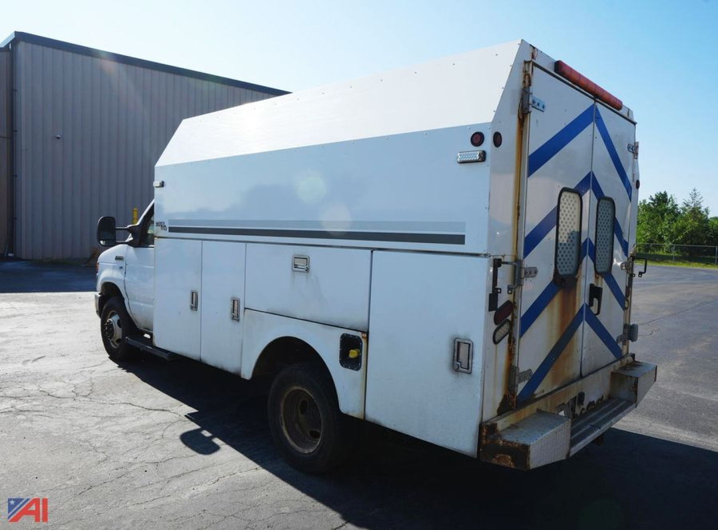 Ford E350 utility truck with white service body and rear double doors parked in lot, side view showing compartments and storage lockers.