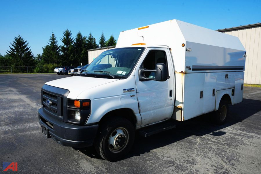 Ford E-350 utility service body truck in white, front three-quarter view showing utility compartments and aluminum utility box on chassis.