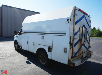 Ford E350 utility truck with white service body and rear double doors parked in lot, side view showing compartments and storage lockers.