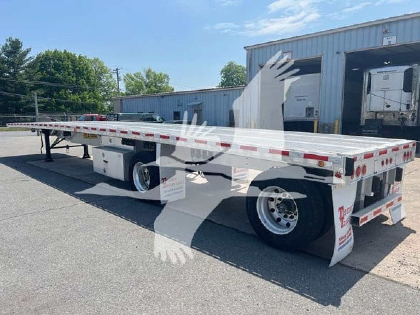 Flatbed trailer showing Maxmiser design with dual rear axles and white reflective tape along sides.