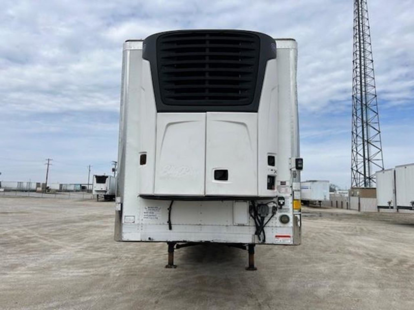 Refrigerated trailer front view showing cargo refrigeration unit and landing legs at a truck yard.