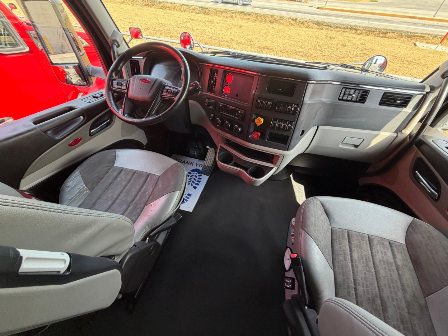 Cab interior of a 2022 Peterbilt 579 conventional sleeper truck showing steering wheel, dashboard, and front seats with gray fabric upholstery.