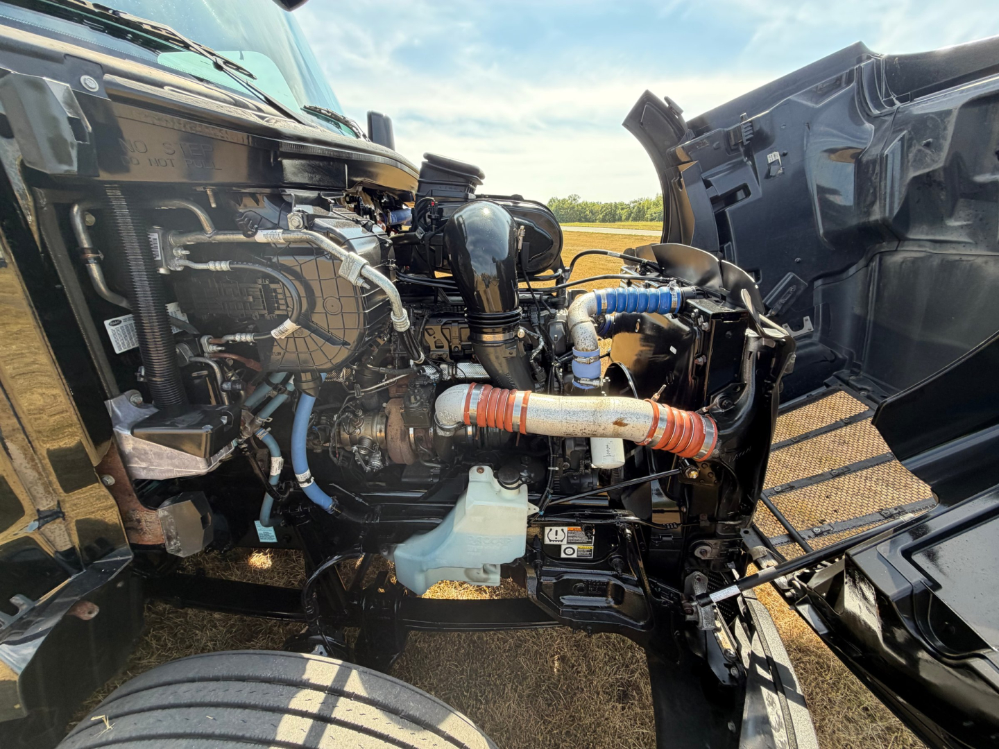 Peterbilt engine bay showing interconnected hoses, metal lines, and various components under an open hood.
