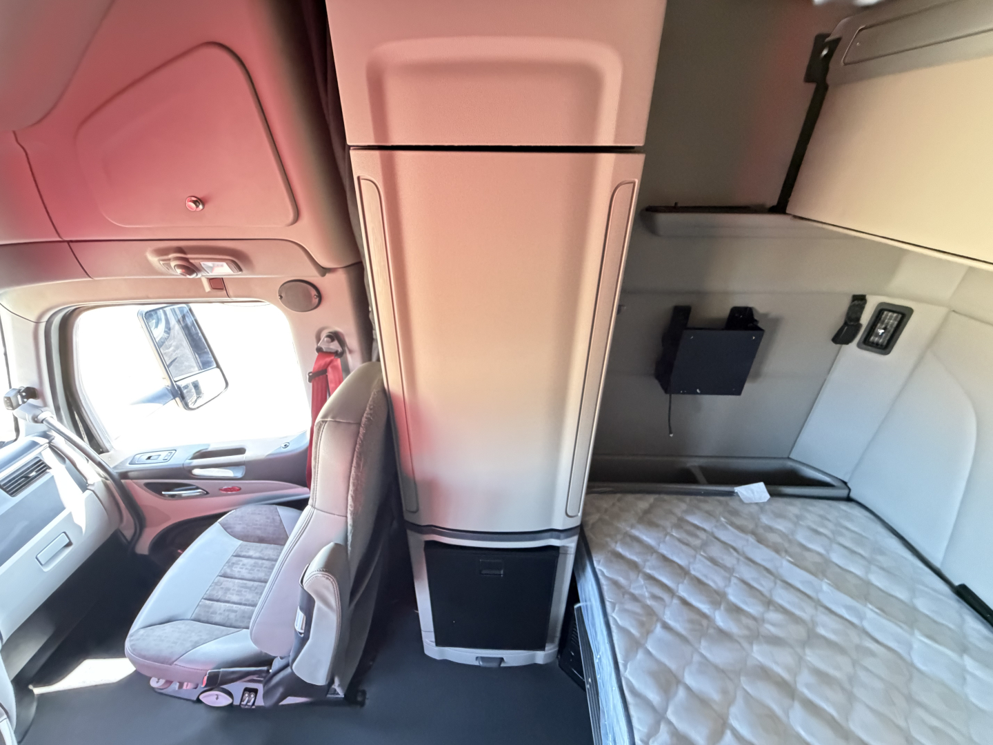 Peterbilt 579 sleeper cab interior showing bunk area and cab storage with light gray upholstery and a padded mattress.