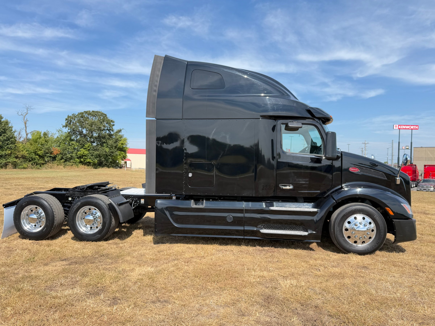 Peterbilt 579 tractor unit side view with black cab and sleeper, three rear axles, chrome wheels, clear sky.