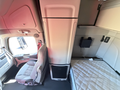 Peterbilt 579 sleeper cab interior showing bunk area and cab storage with light gray upholstery and a padded mattress.