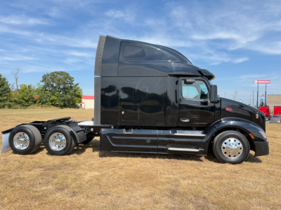 Peterbilt 579 tractor unit side view with black cab and sleeper, three rear axles, chrome wheels, clear sky.