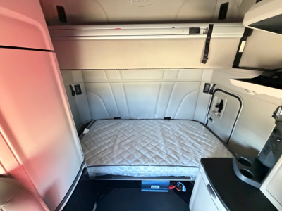 Cab interior of a 2022 Peterbilt 579 sleeper truck showing a padded mattress in the sleeper compartment and surrounding cabinets.
