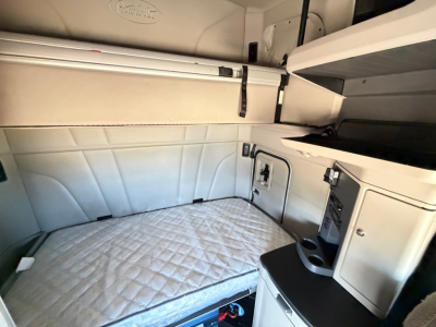 Peterbilt 579 sleeper cab interior with bunk bed and storage compartments visible, light gray upholstery and built-in galley features.