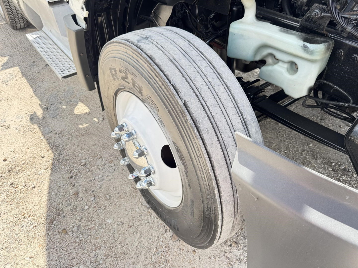 Front wheel view of a 2018 International LT truck showing a dual-axle front wheel with tire, wheel bolts, and nearby coolant reservoir.