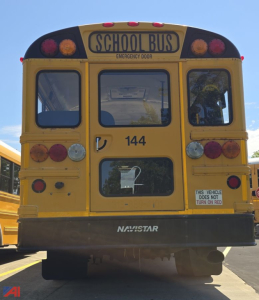 School bus rear view showing 144 and wheelchair lift; BY Navistar logo on rear bumper; emergency door label and vehicle does not turn on red notice.