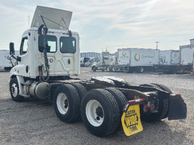 Truck chassis and cab of a 2018 Freightliner Cascadia 113 conventional daycab showing rear wheel axles and fifth-wheel area with yellow caution sign on mudflap.