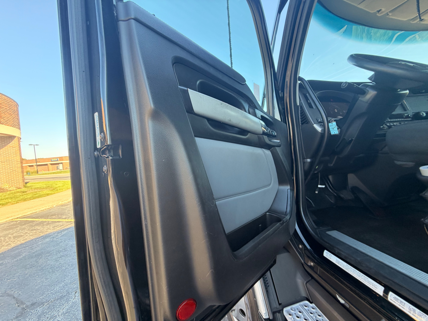 Truck cab interior door panel view of a Kenworth T680 with light gray and black door trim and window switch area.