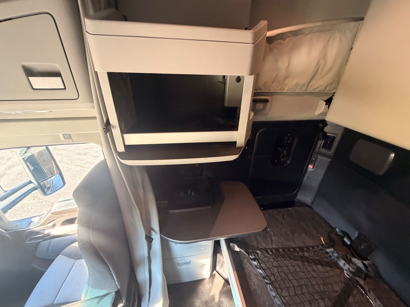Kenworth T680 interior cabin area showing sleeper compartment and small table with storage drawers visible.