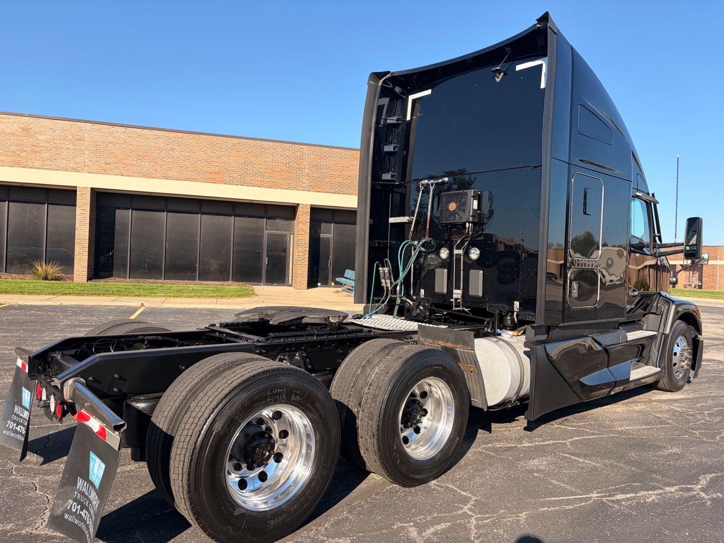 Kenworth T680 tractor in-service with exposed chassis showing fuel tanks and side-mounted exhaust, rear triple-axle configuration, black glossy cab.