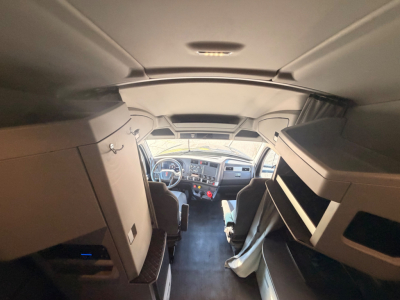 Kenworth T680 cabin interior view from doorway showing dashboard, steering wheel, and bunk storage.