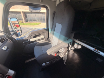 Kenworth T680 cab interior showing driver seat and dash area with bunk area in background.