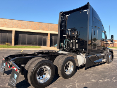 Kenworth T680 tractor in-service with exposed chassis showing fuel tanks and side-mounted exhaust, rear triple-axle configuration, black glossy cab.