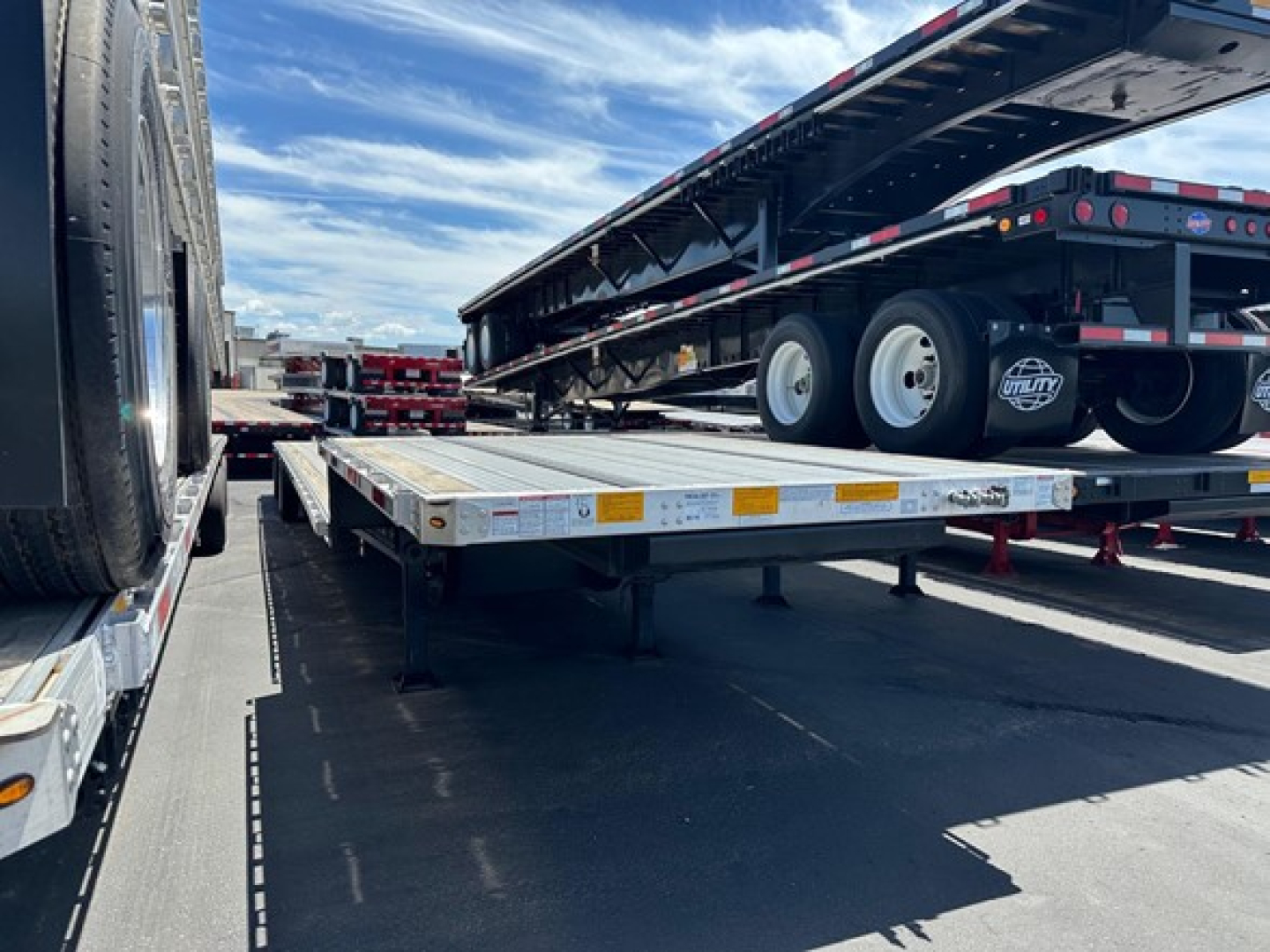 Trailer with a drop deck design showing a long flatbed with dual axles and a spare tire, stock number and winch presence not visible.