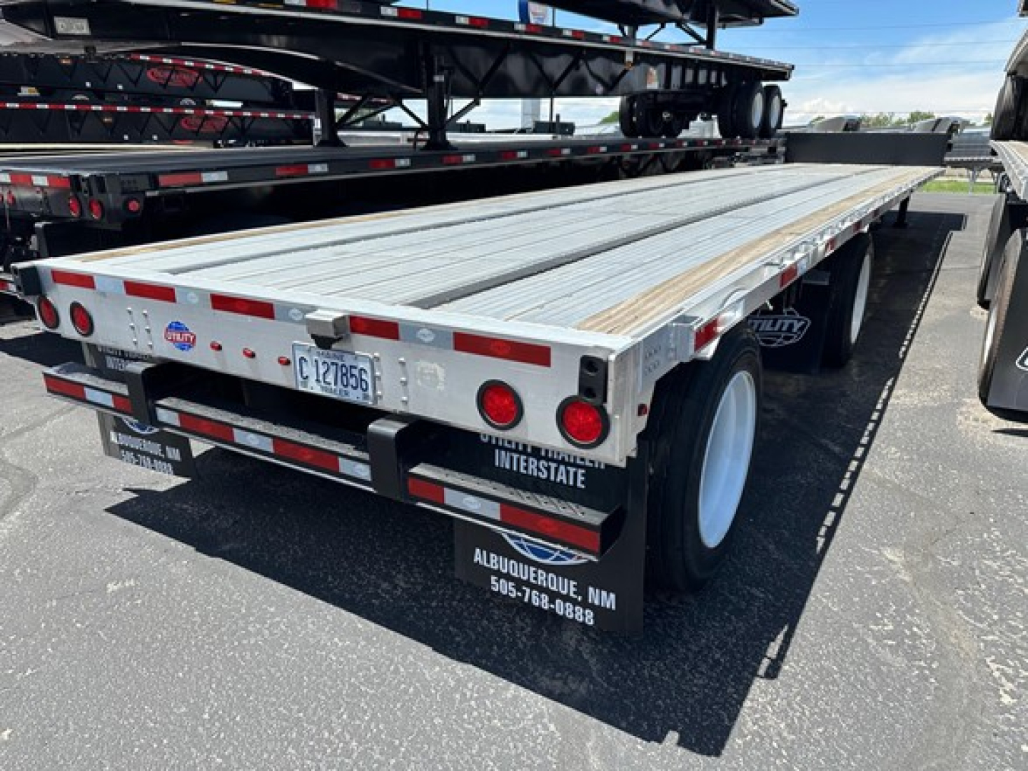 Flatbed trailer rear view showing aluminum deck and dual axle, with red reflectors and ‘Albuquerque NM 505-768-0888’ mudflaps.
