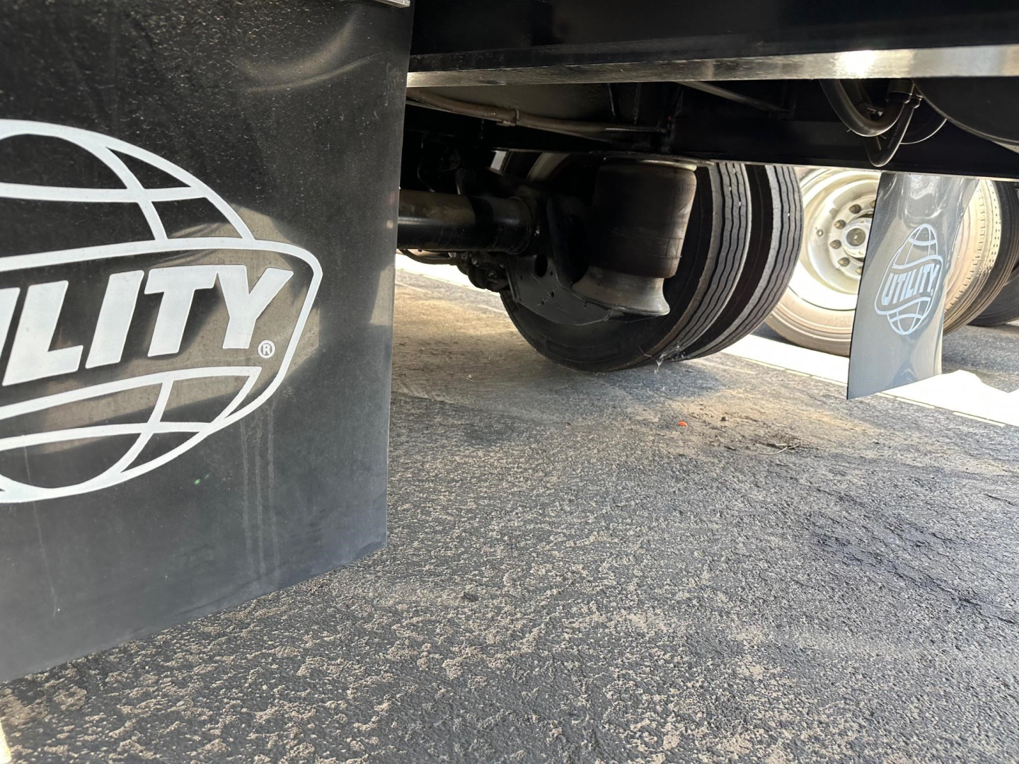 Under view of a Utility 4000AE combo drop deck trailer showing dual rear axles, tires, and mud flaps with Utility logo visible.