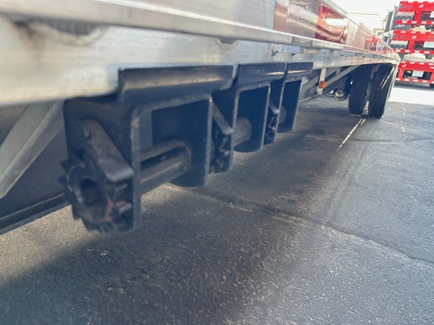 Underneath a utility trailer showing the undercarriage support hooks and mounting brackets along the side of a drop deck.