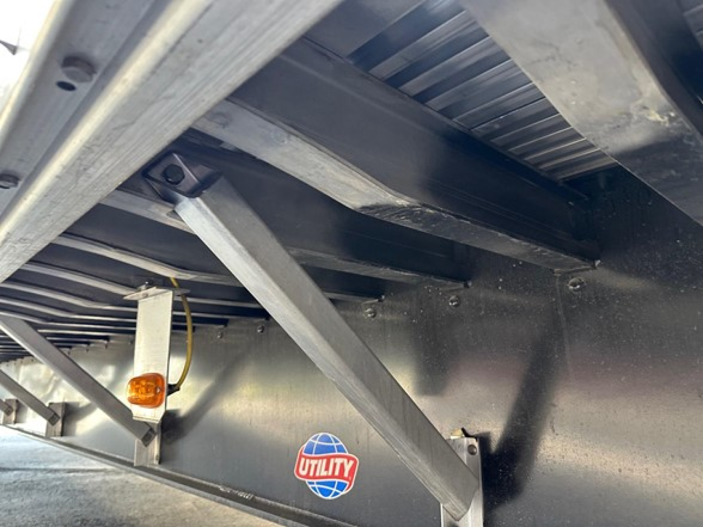 Utility trailer underside showing structural beams and a side marker light with Utility logo on the deck, visible frame and support brackets.