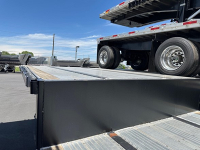 Trailer bed with drop deck showing steel deck and a raised tractor/tandem axle near the rear in a used trailer yard.