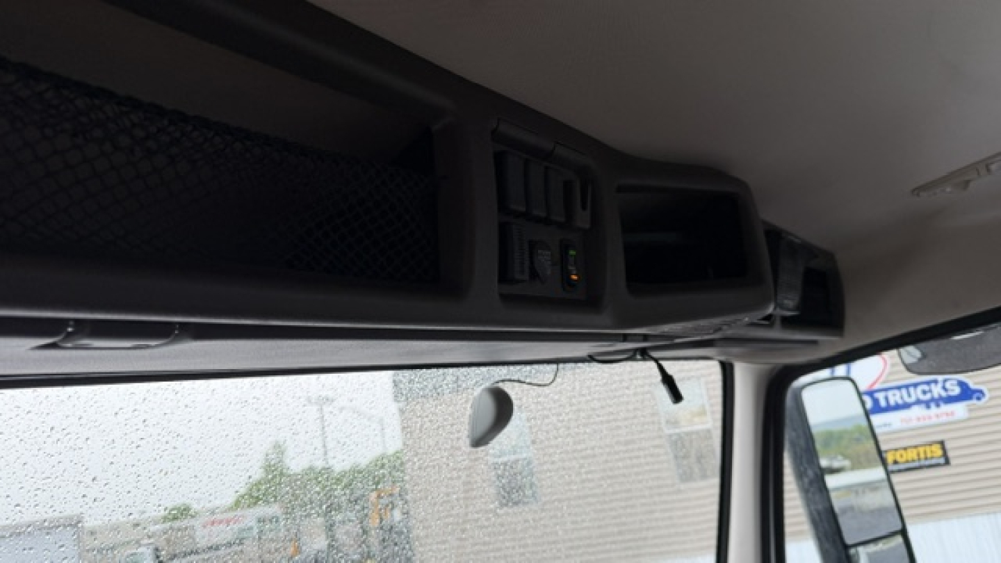 Dashboard area of a Volvo truck cab showing overhead storage and dashboard controls with window view.