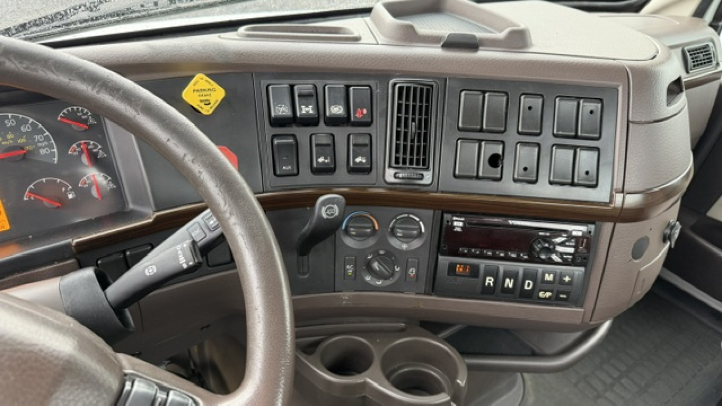 Volvo VNL64T300 cab interior showing dashboard switches, steering wheel, and instrument cluster with climate controls and gear selector.
