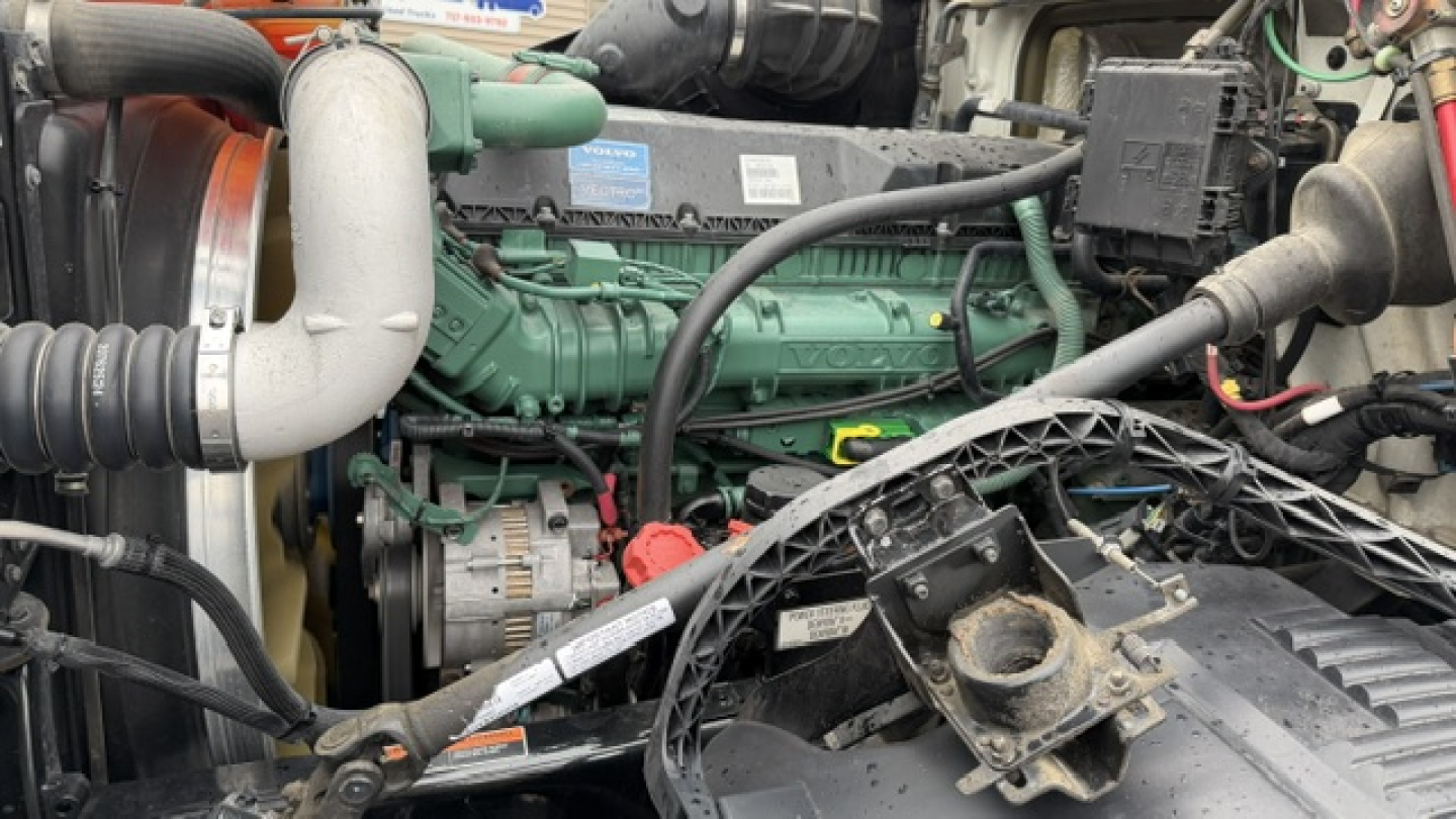 Volvo VNL64T300 engine bay view with green diesel engine, belts, hoses, and components visible.