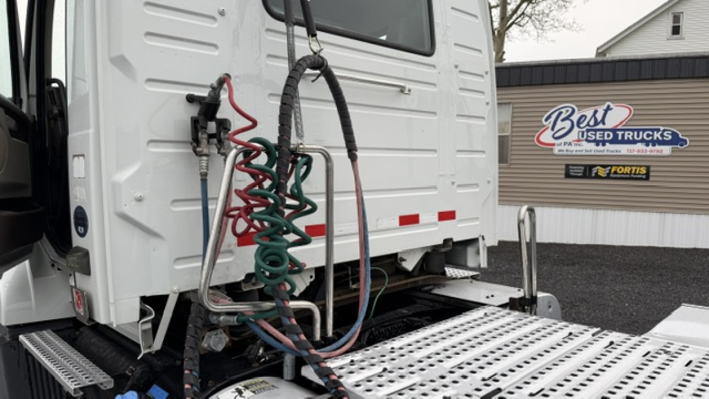 Rear view of a 2016 Volvo VNL64T300 cab with coiled air lines and electrical cables mounted on the back, showing bumper step and access panel.