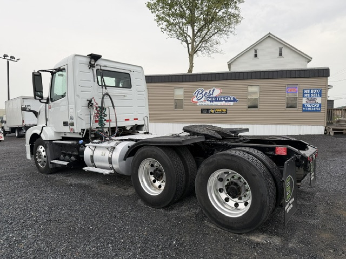 Volvo VNL64T300 tractor rear view showing dual rear axles and fuel tank; company signage on building in background.