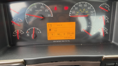 Volvo VNL dash cluster showing multiple gauges and a yellow/orange display with warning icons and text; visible labels include speedometer, tachometer, and fuel/engine indicators.
