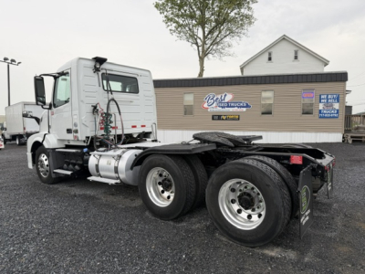 Volvo VNL64T300 tractor rear view showing dual rear axles and fuel tank; company signage on building in background.