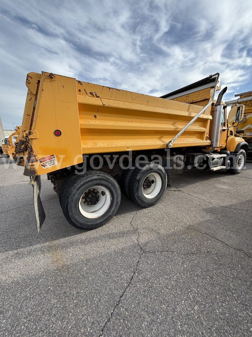 Dump truck bed of a yellow 2003 Mack CV713 in-service with side panels and dual rear wheels.