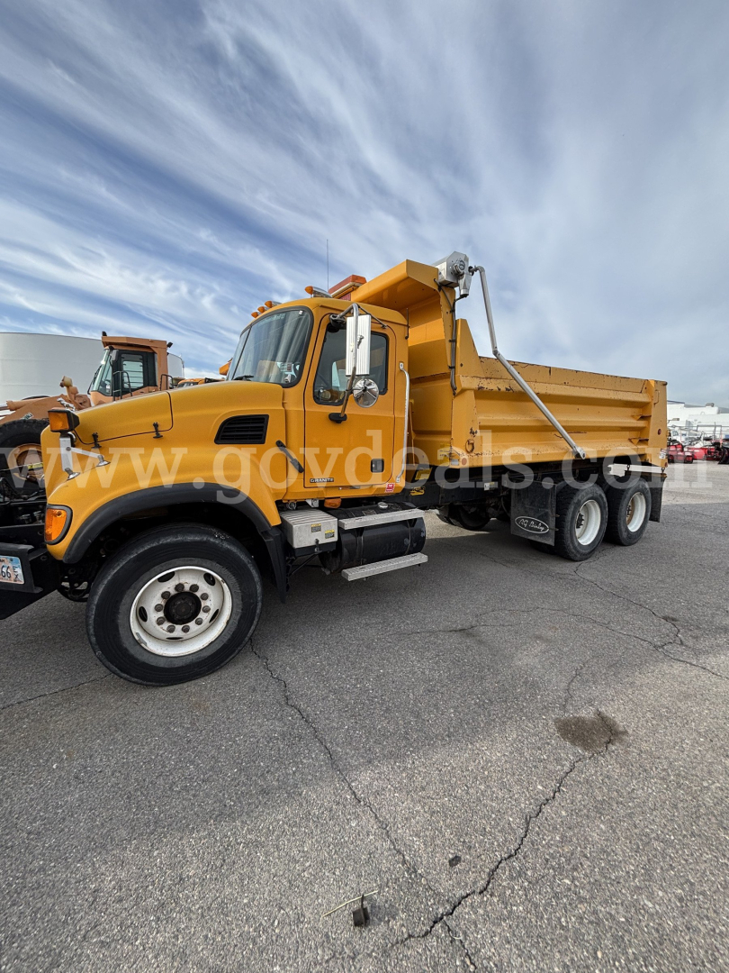 Mack CV713 dump truck in service showing cab and dump bed with hydraulic hoist and wheel setup.