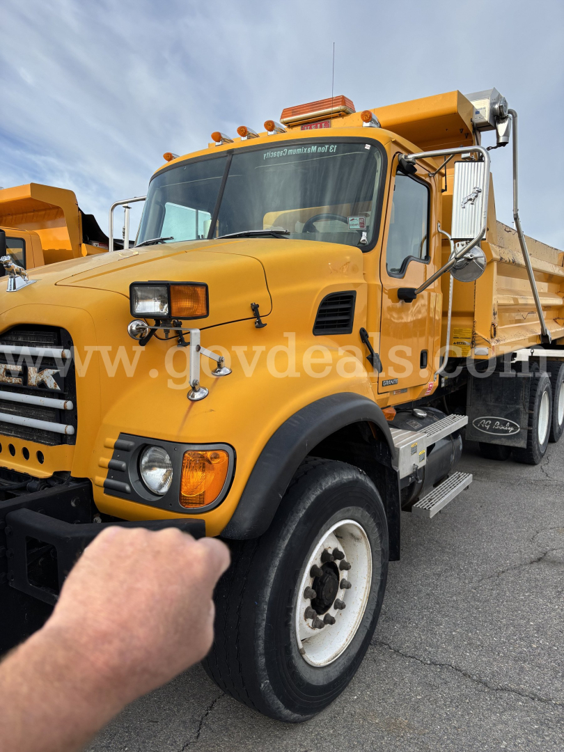 Mack CV713 dump truck in-service showing front left view with yellow cab and black bumper, marker lights and side mirrors.