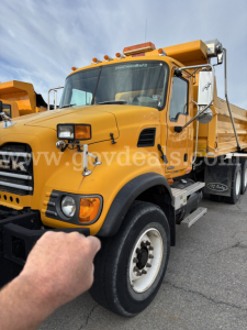 Mack CV713 dump truck in-service showing front left view with yellow cab and black bumper, marker lights and side mirrors.