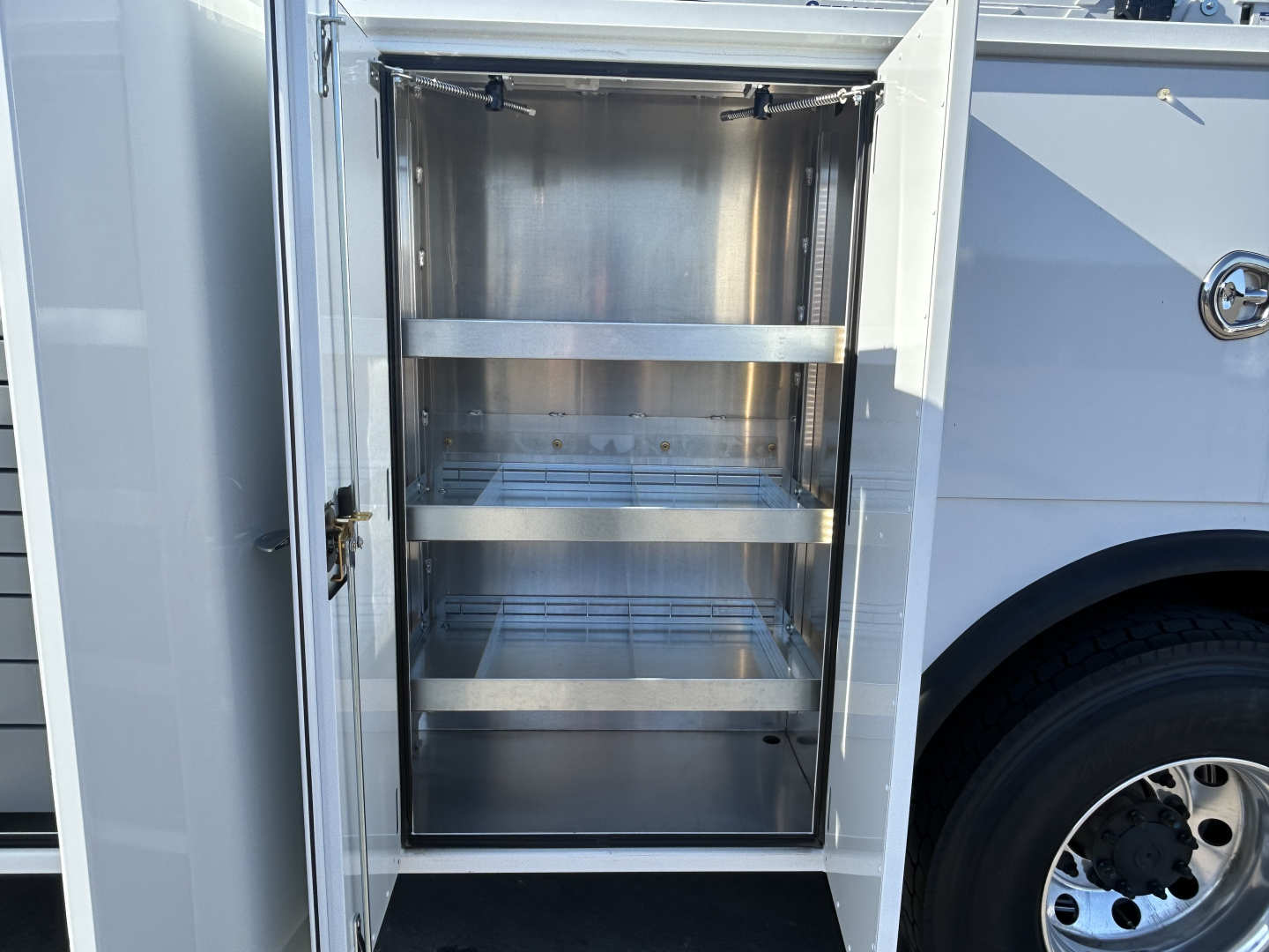 Utility truck body compartment with empty metal shelving in open storage locker inside a Mack MD7 truck.