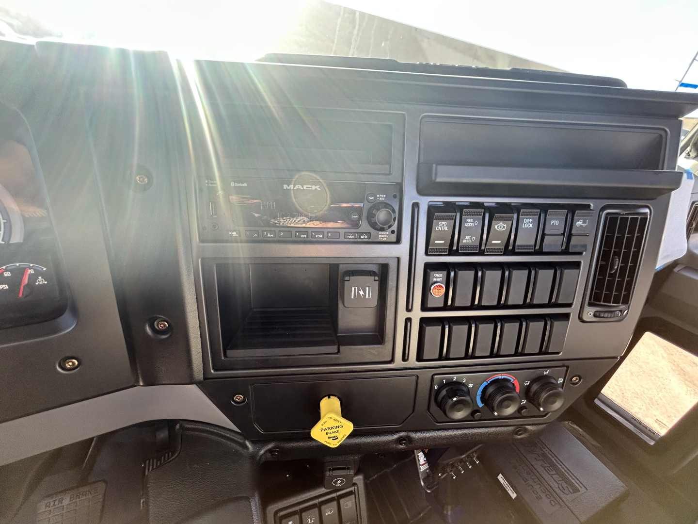 Truck dash panel showing radio, numerous toggle switches, climate controls, and a yellow hood release lever visible in a Mack MD series truck interior.