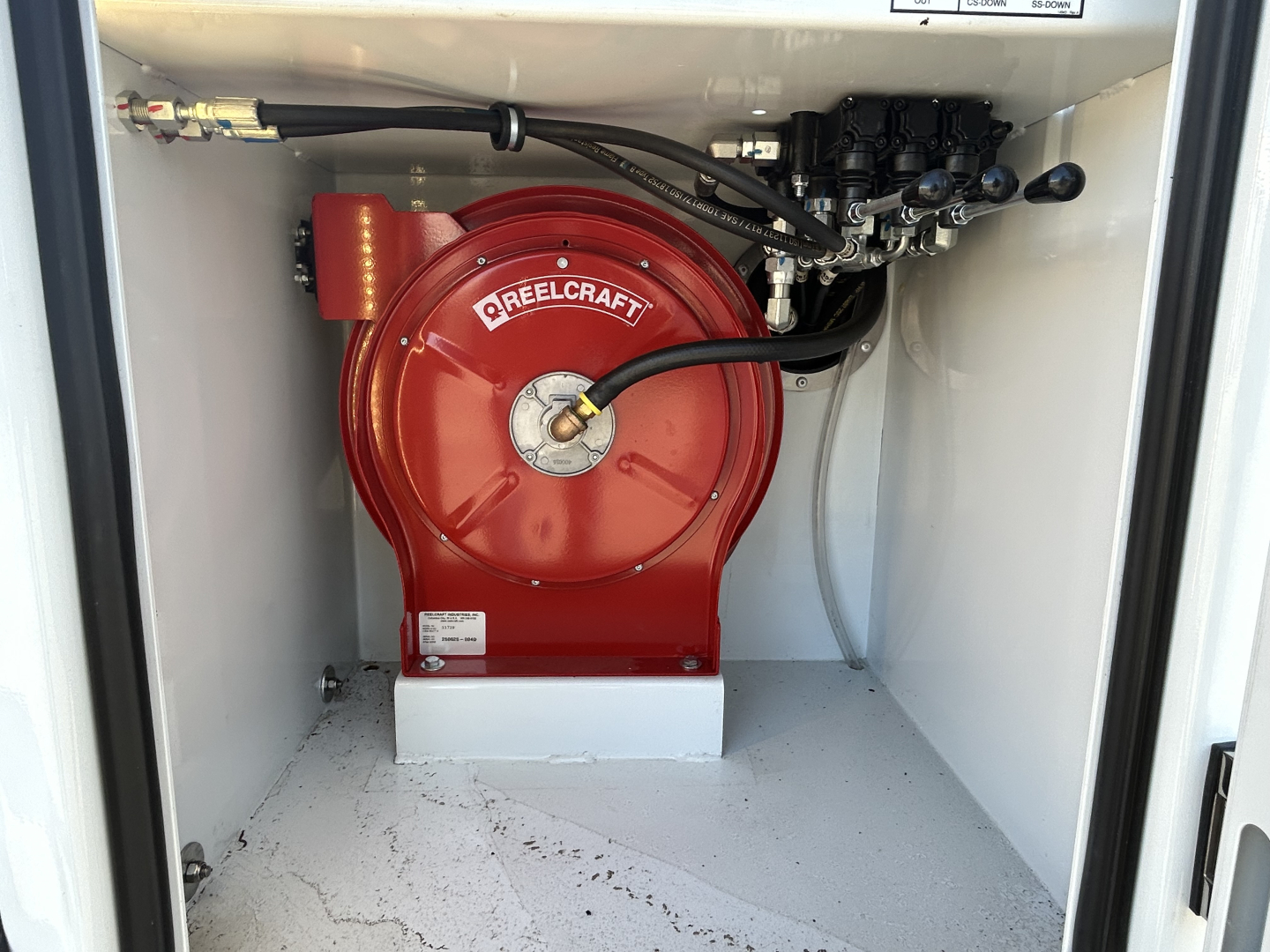 Red REELCRAFT hose reel in a white utility truck compartment with hoses and control valves visible.