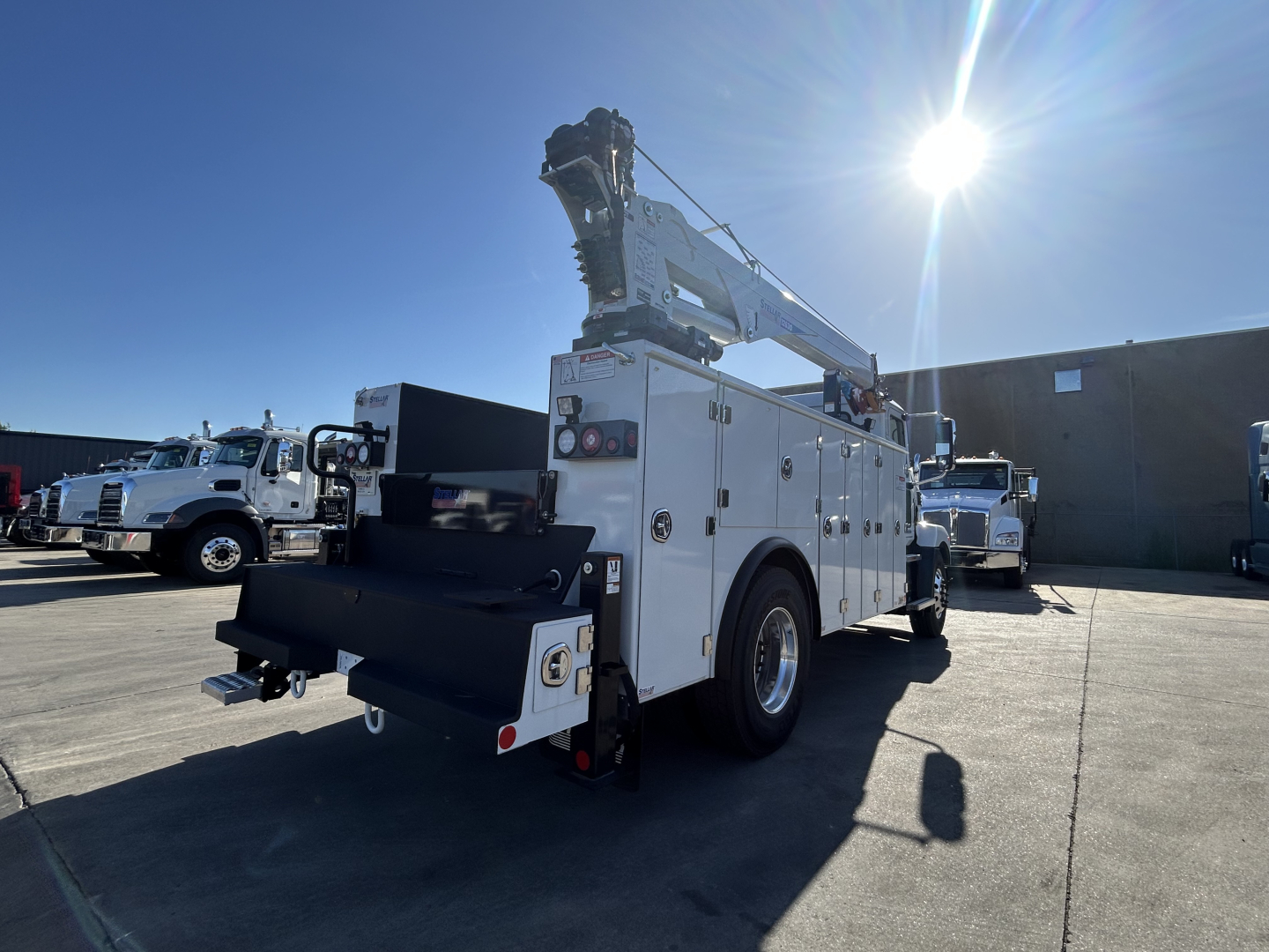 Mack MD7 utility truck with hoist and service body, rear side view showing crane and storage compartments.