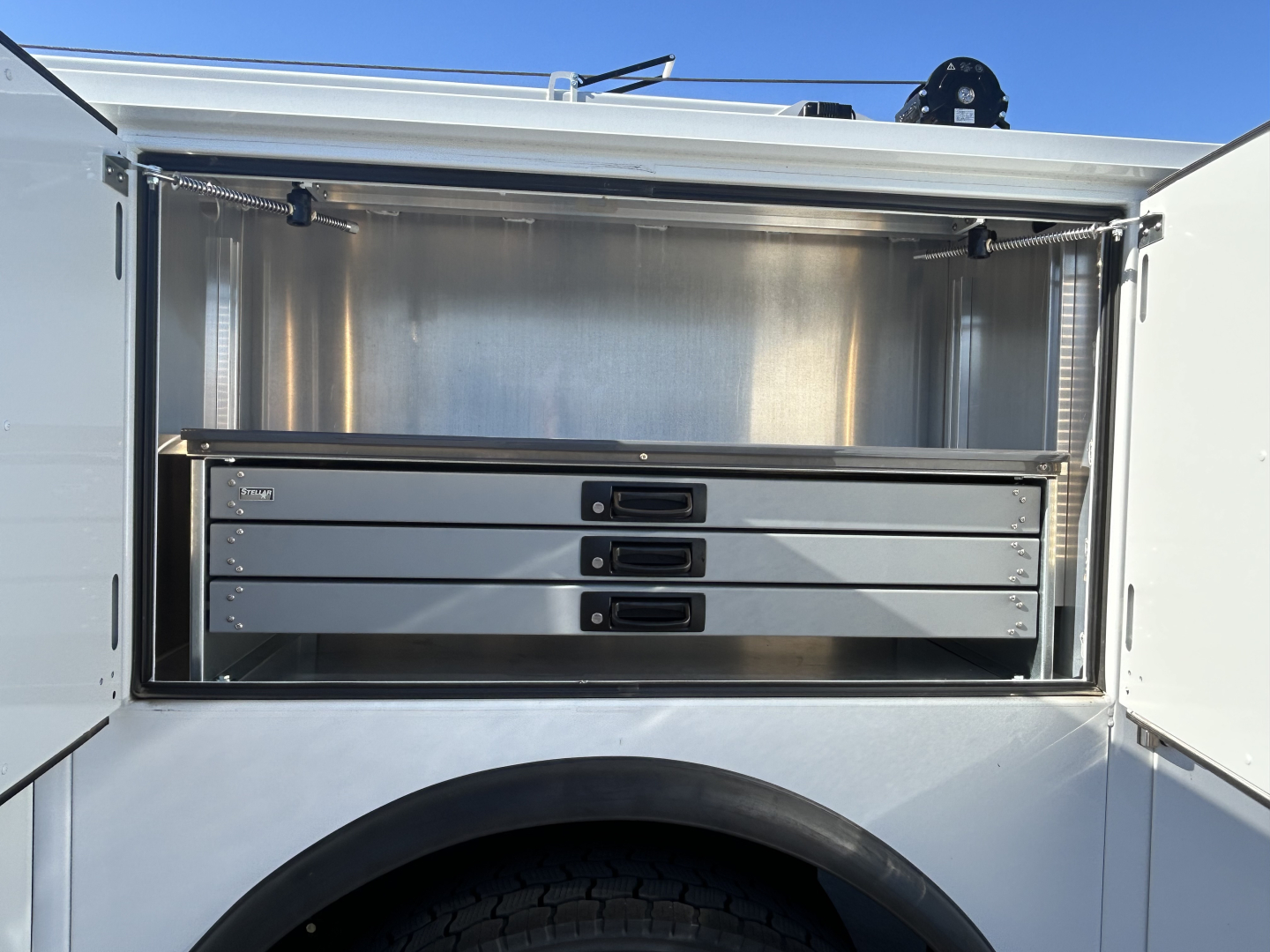 Service body storage compartment on a 2025 Mack MD7, showing four slide-out steel drawers inside a metal cargo bay with latching handles.