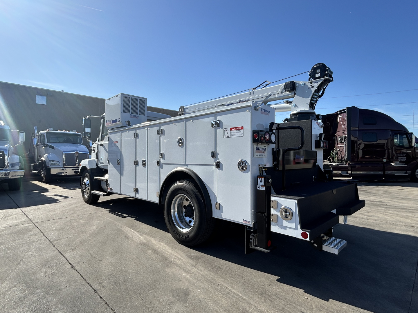 Mack MD7 service truck in a parking lot showing utility body with compartments and cherry picker arm folded at rear.