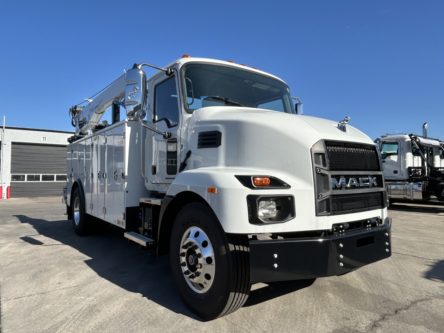 Mack MD7 service truck in white showing front grille with MACK logo and large bumper, side compartments, crane on cab roof, and dual rear wheels.