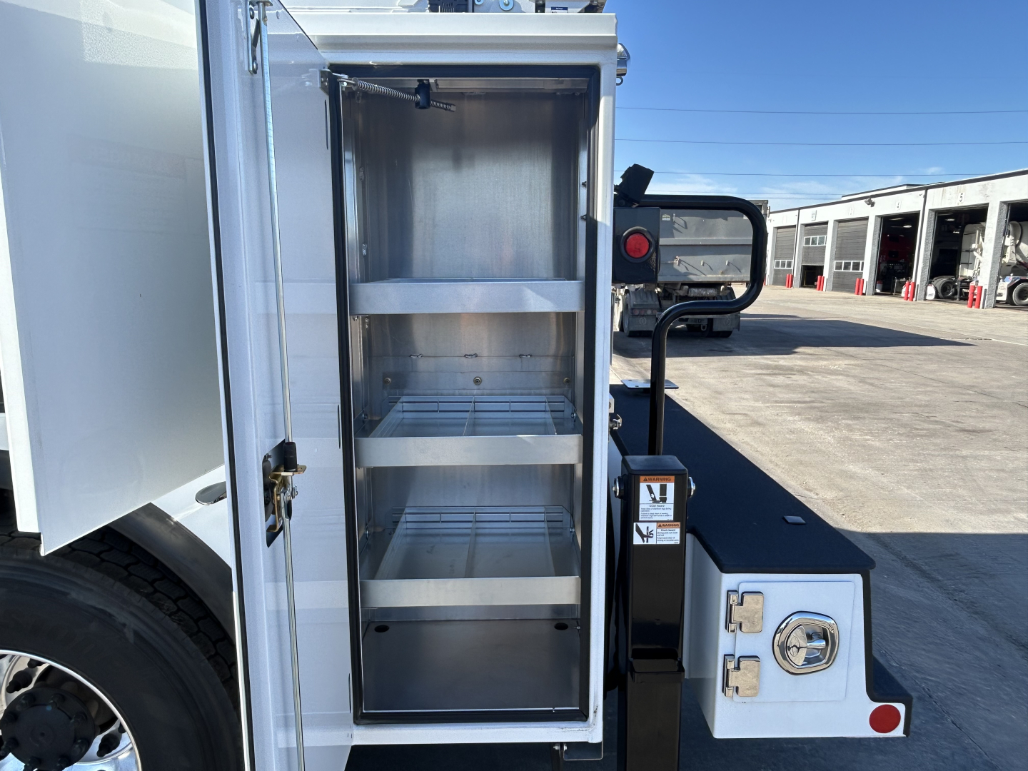 Mack MD7 service truck rear storage cabinet open showing multiple empty shelves.