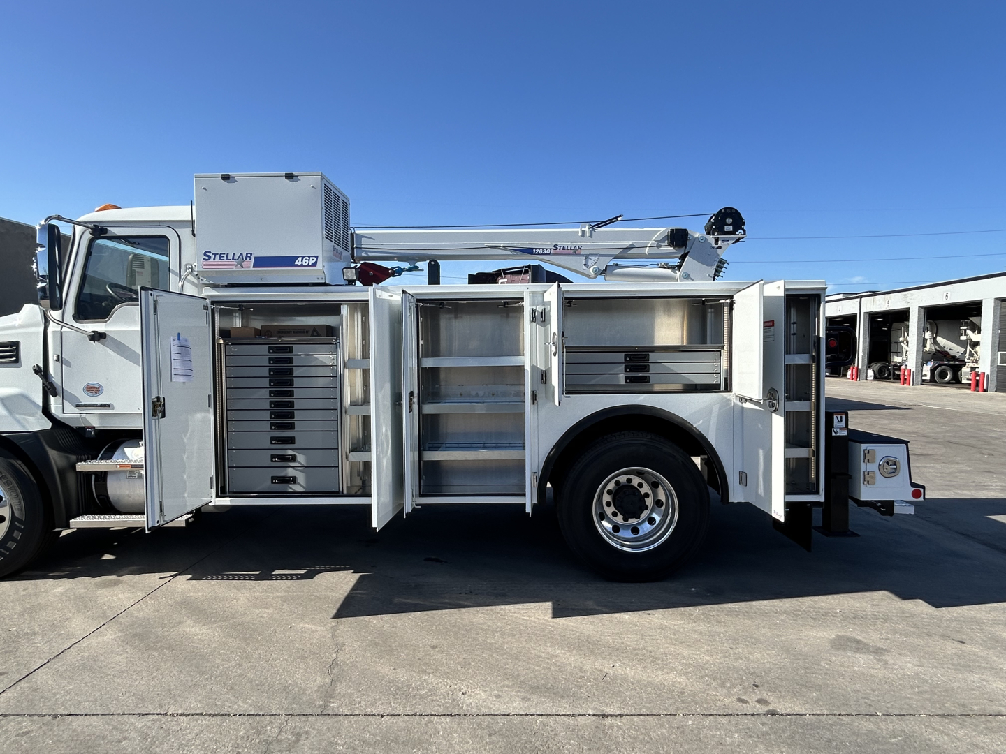 Mack MD7 service truck side view with multiple open compartments showing tool/storage lockers and hydraulic boom in the truck bed.