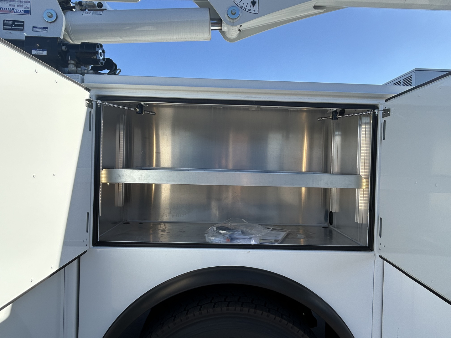 Service/utility truck bed compartment open showing empty stainless storage box with a divider shelf in a new Mack MD7 truck.